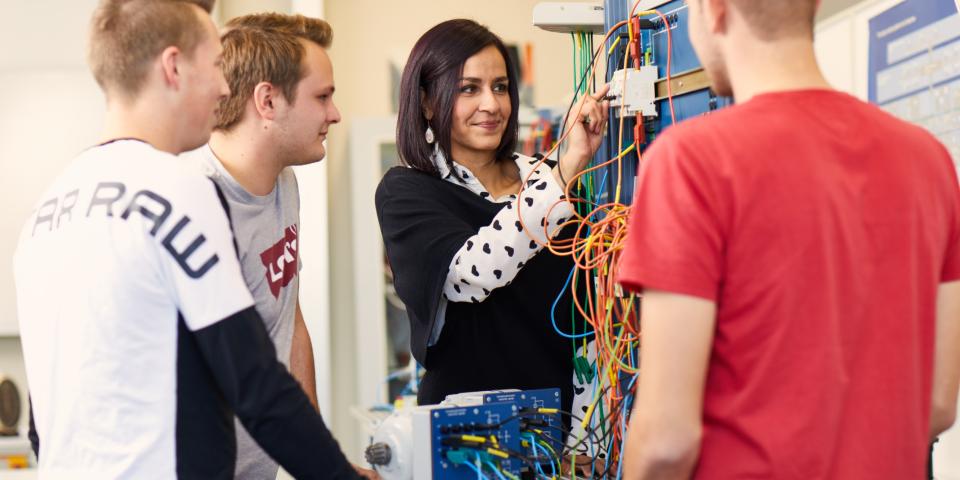 Lehrerin erklärt Schülern im naturwissenschaftlichen Unterricht eine eletronische Aparatur.