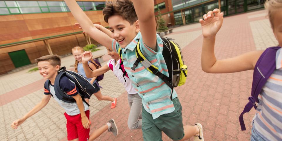 Schülerinnen und Schüler laufen fröhlich über einen Schulhof.