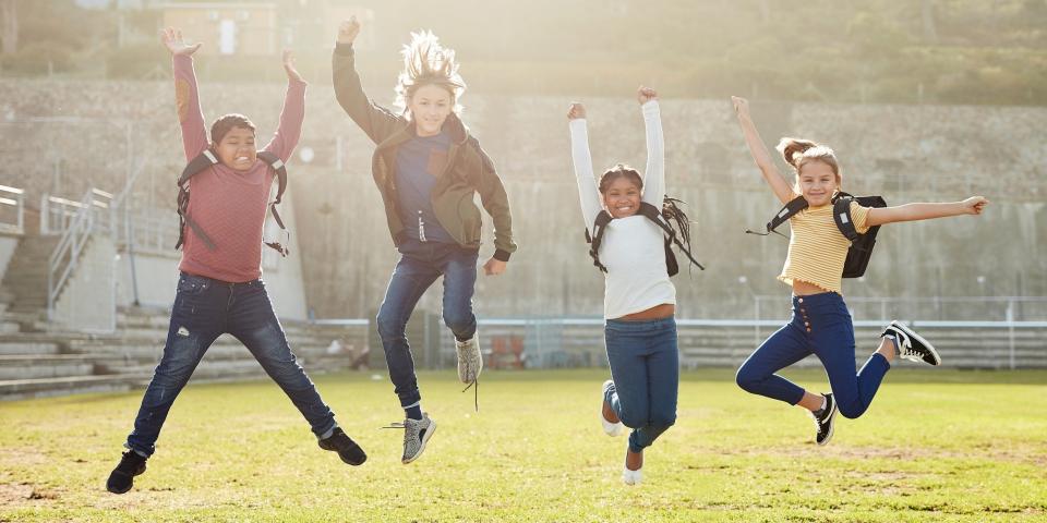 Eine Gruppe Kinder springt auf einer Wiese in die Luft.