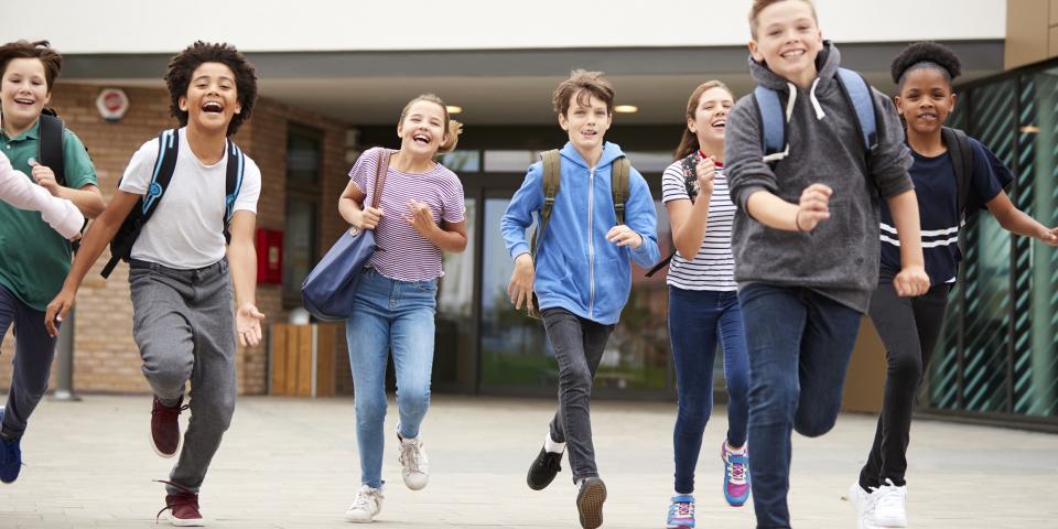 Schüler laufen lachend aus Schulgebäude.