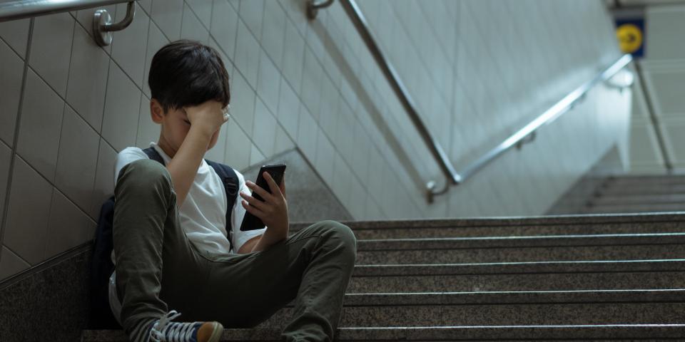 Junge sitzt mit seinem Smartphone in der Hand auf einer Treppe