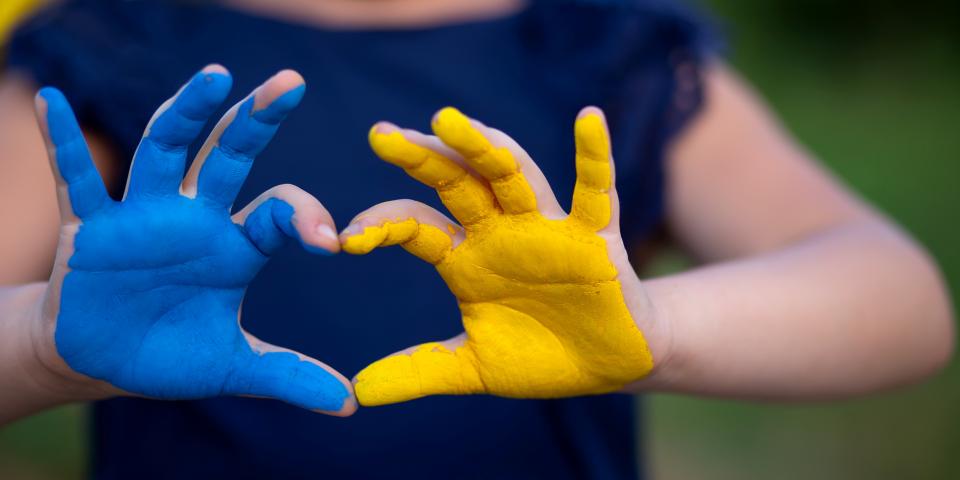 Blau und gelb bemalte Hände formen ein Herz