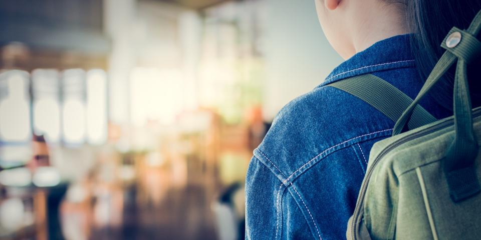 Rückansicht eines Mädchens mit Rucksack vor einem Klassenraum.