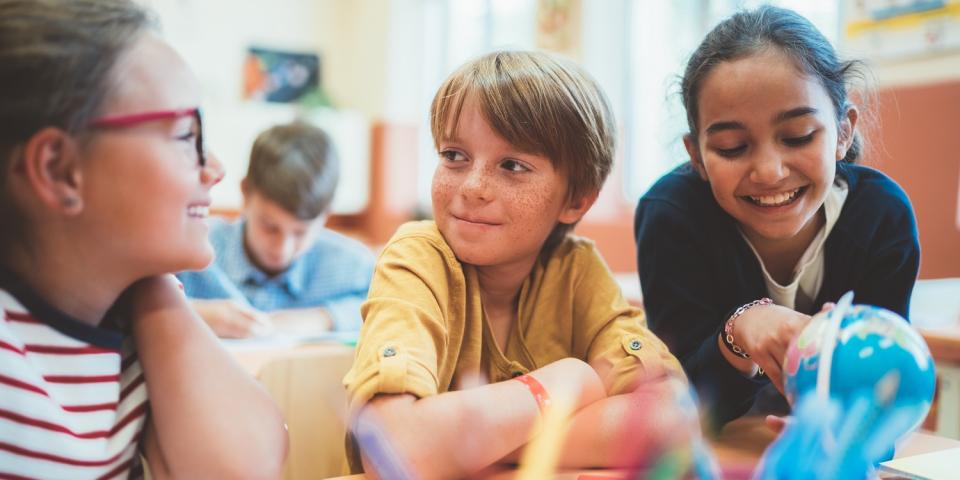 Grundschülerinnen und Grundschüler sitzen an einem Tisch im Unterricht und bearbeiten gemeinsam eine Aufgabe.