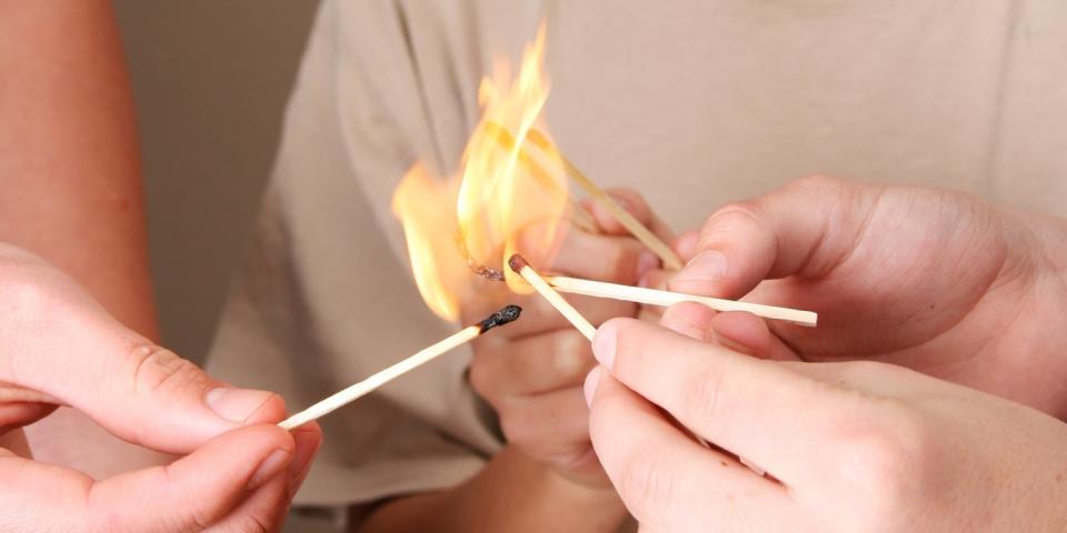 Mehrere Hände halten brennende Streichhölzer zusammen, zu erkennen ist in der Mitte nur ein Kind, das ebenfalls ein Streichholz in die große Flamme streckt. 