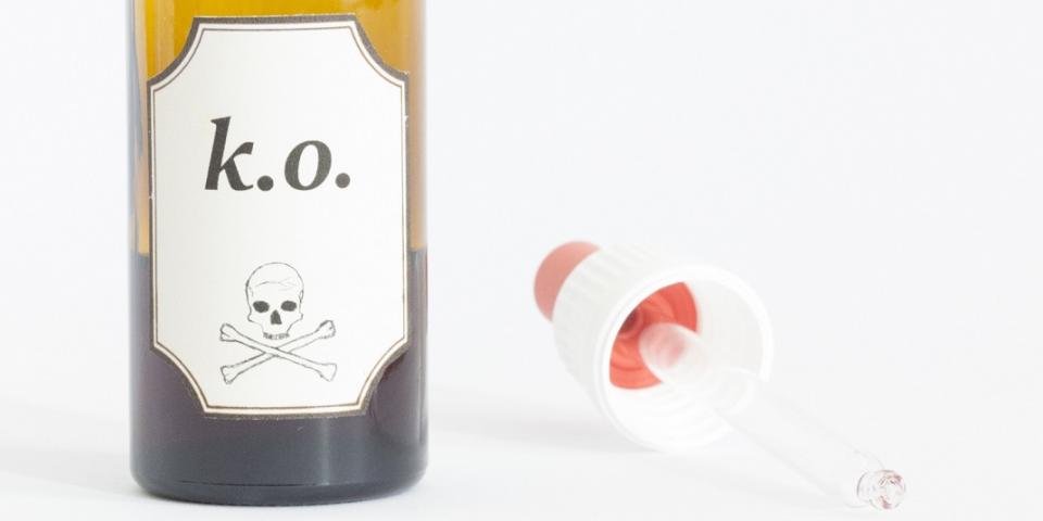 Eine Pipette liegt neben einem geöffneten Glasfläschen mit einem Etikett mit der Aufschrift "k.o." sowie einem Totenkopf.