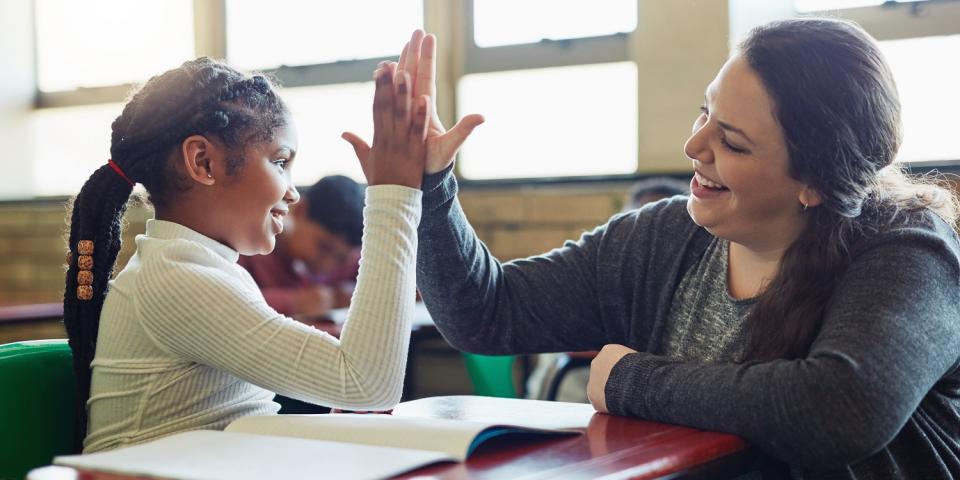 Schülerin und Lehrerin berühren ihre Hände in einer "High Five"-Geste. Beide lächeln dabei.