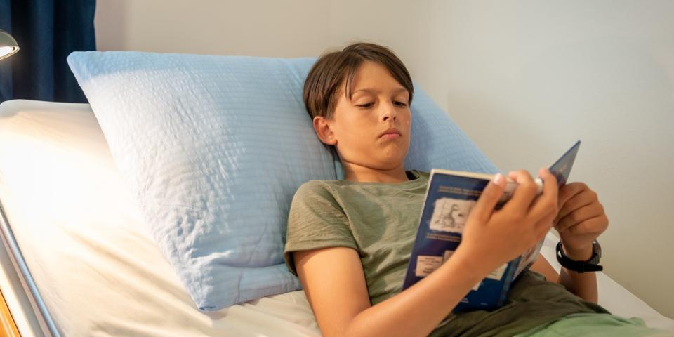Ein Junge liegt in einem Krankenbett und liest in einem Buch