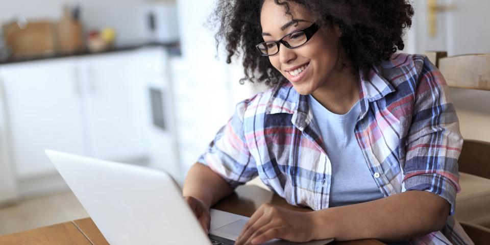 Eine Frau sitzt an einem Tisch und blickt in einen geöffneten Laptop.