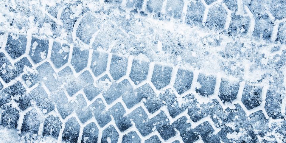 Detailaufnahme von Reifenspuren auf einer eisigen, verschneiten Straße.