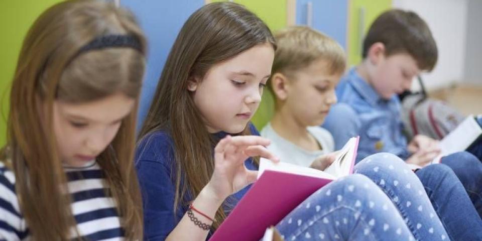 Grundschulkinder, die auf dem Boden sitzen und in Büchern lesen.