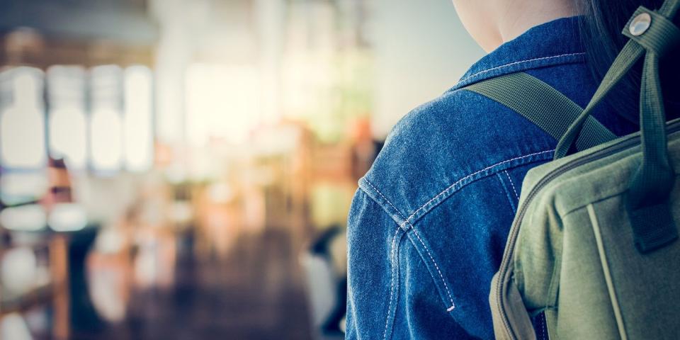 Schülerin mit Rucksack schaut auf einen leeren Schulflur