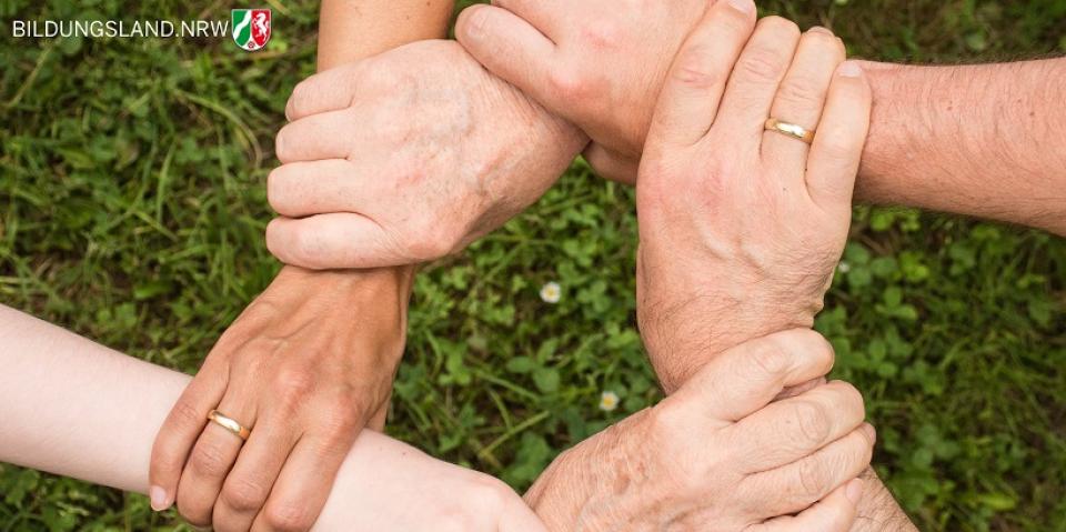 Hände verschiedener Generationen sind über einer Rasenfläche zu einem Geflecht verschränkt