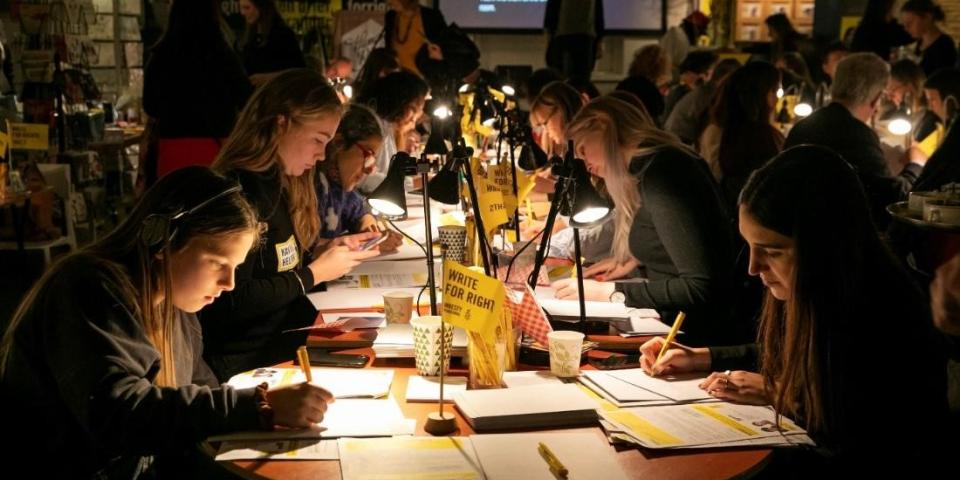 Schülerinnen und Schüler sitzen mit Leselampen an Tischen und schreiben Briefe im Rahmen des Briefmarathons von Amnesty International.