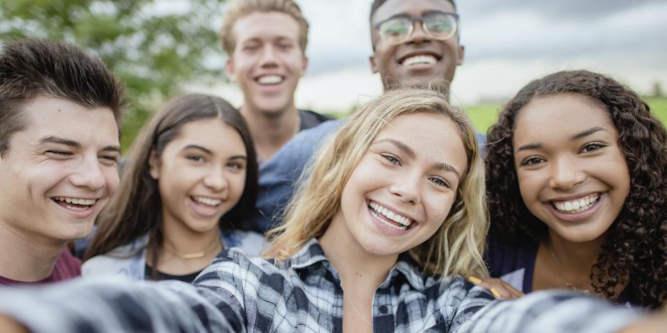 Selfie-Perspektive auf mehrere junge Menschen, die sich lächelnd zum Foto gruppiert hat.