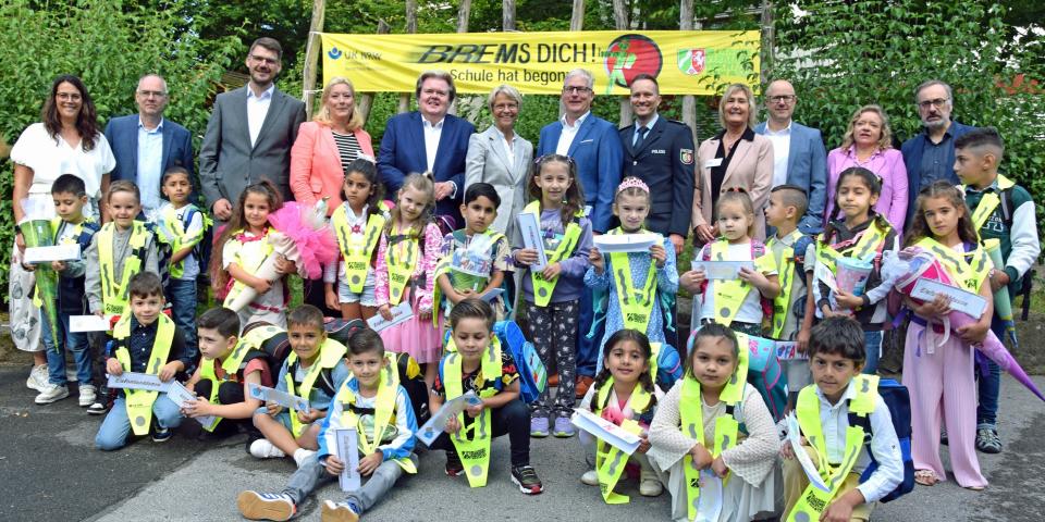 Gruppenbild von Ministerin Dorothee Feller mit Vertreterinnen und Vertretern der Landesverkehrswacht und Schülerinnen und Schülern, im Hintergrund ein Banner mit der Aufschrift "Brems Dich! Schule hat begonnen!"