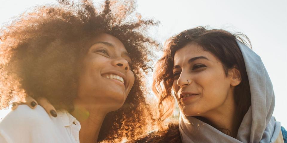 Zwei Frauen mit Migrationshintergrund stehen eng beisammen, eine der beiden trägt ein lockeres Kopftuch.