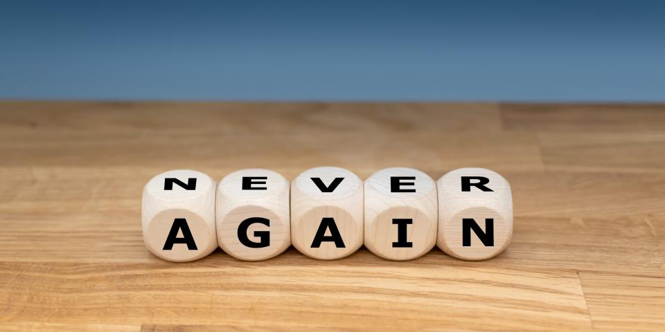 Auf einer Holzplatte liegen fünf Buchstabenwürfel, die die englischen Worte "NEVER" und "AGAIN" bilden.