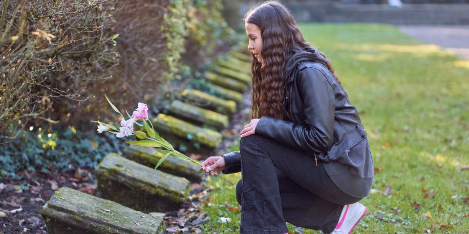 Eine Schülerin legt Blumen auf einem Grab einer Gedenkstätte nieder.