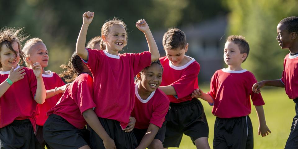 Kinder in Sport-Trikots stehen jubelnd zusammen.