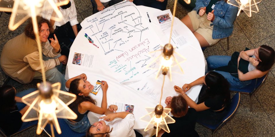 Junge Menschen sitzen gemeinsam um einen Tisch und arbeiten zusammen im Projekt MILeNa.