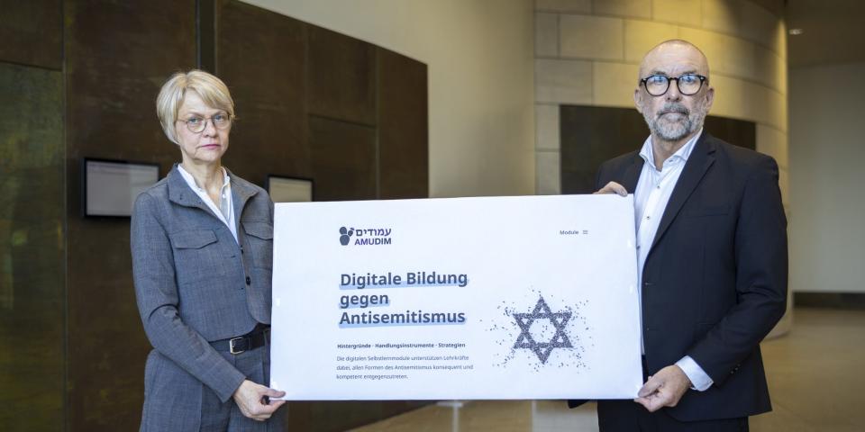 Ministerin Feller und Bert Römgens präsentieren ein Plakat zum Start von AMUDIM (25. Februar 2026)