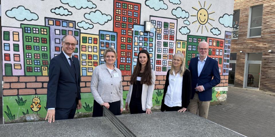 An der Südparkschule Gladbeck stehen Sts Dr. Mauer, Schulleiterin Viola Beyer, Laura Theben (erweiterte Schulleitung, Klassenlehrerin), Natascha Stahl von der Schulaufsicht Recklinghausen, Martin Teuber, Referatsleiter 33 im MSB an einer Tischtennisplatte.