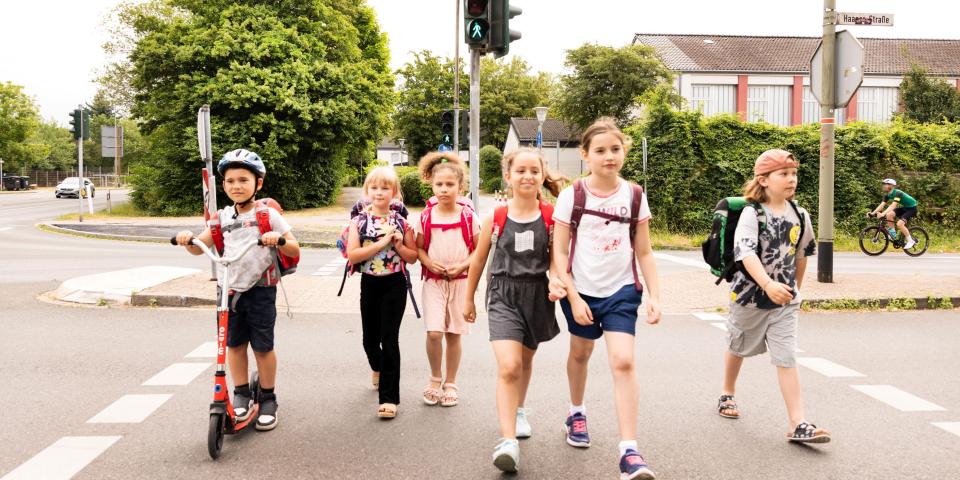 Eine Gruppe Kinder mit Tornistern überquert eine Straße.