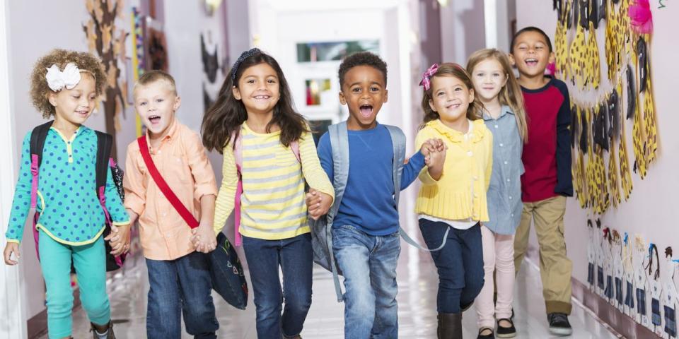 Vorschulkinder laufen Hand in Hand durch einen Schulflur.