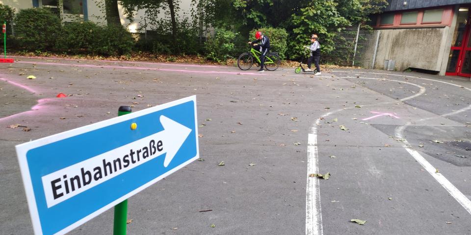Kinder auf Fahrrädern, im Vordergrund ein Einbahnstraßen-Schild