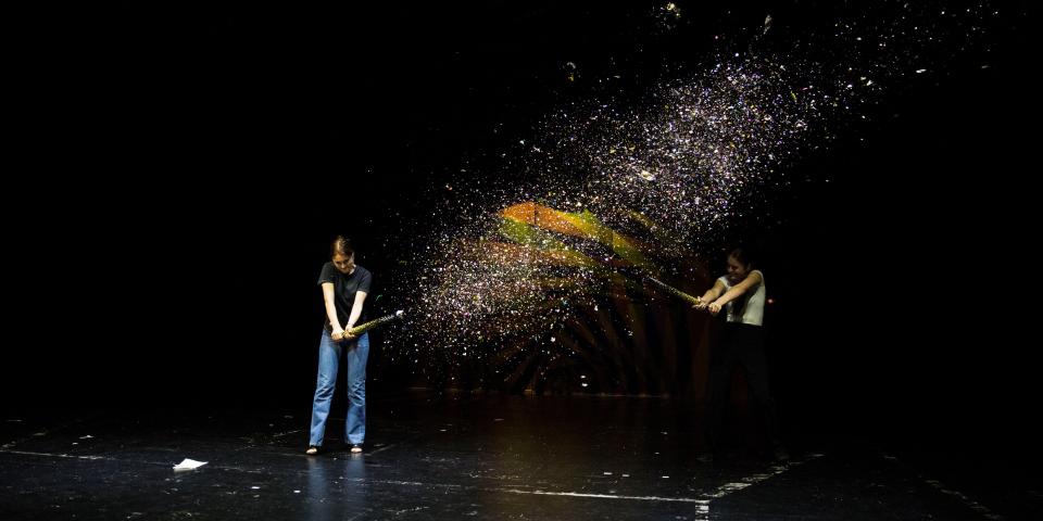 Zwei junge Frauen starten Konfettikanonen auf einer großen Theaterbühne.