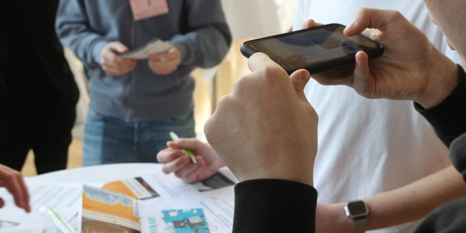 Mehrere Menschen stehen an einem Tisch, dabei macht eine Person ein Foto mit einem Smartphone.