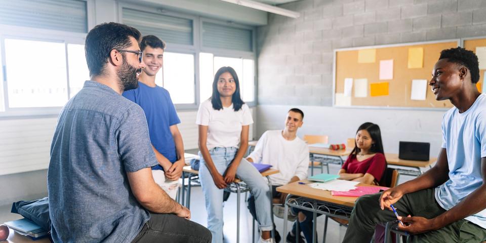 Schülerinnen und Schüler diskutieren mit einem Lehrer.