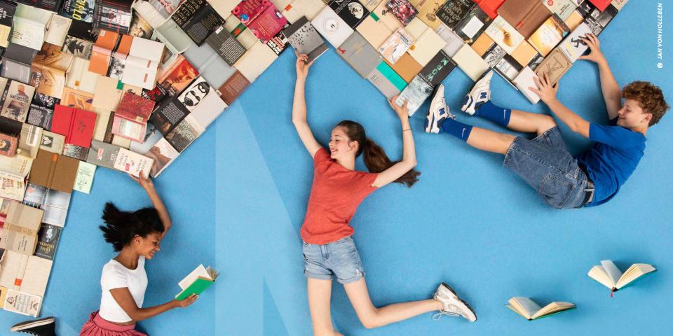 Das Plakat zum Vorlesewettbewerb zeigt zwei liegende Kinder mit vielen Büchern.