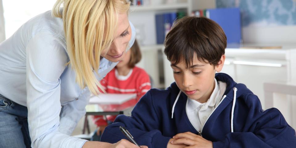 Eine Lehrerin beugt sich im Unterricht helfend über einen Schüler.