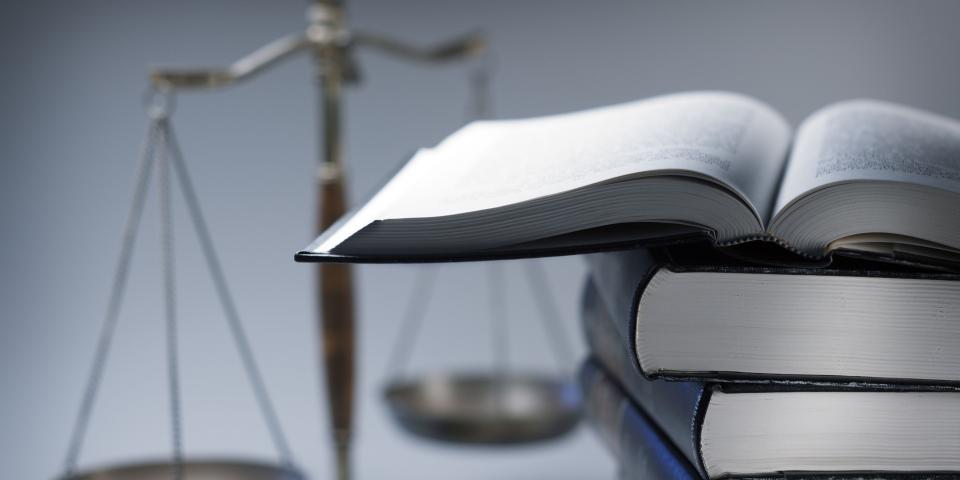 Symbolbild Recht: Im Vordergrund ein Stapel Bücher, im Hintergrund eine Waage.
