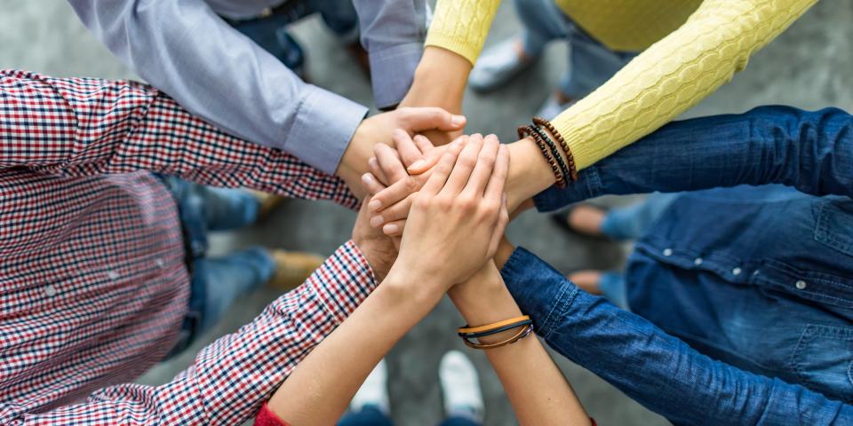 Fünf Menschen stehen im Kreis und legen ihre Hände aufeinander, die Gesichter sind nicht zu erkennen.