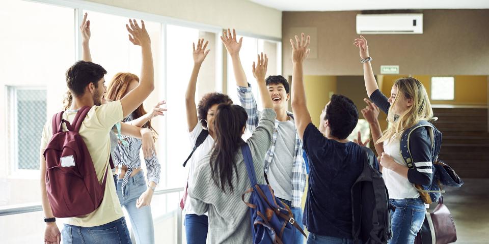 Eine Gruppe Schüler steht in einem Schulflur und hat die Hände zum "High Five" erhoben.