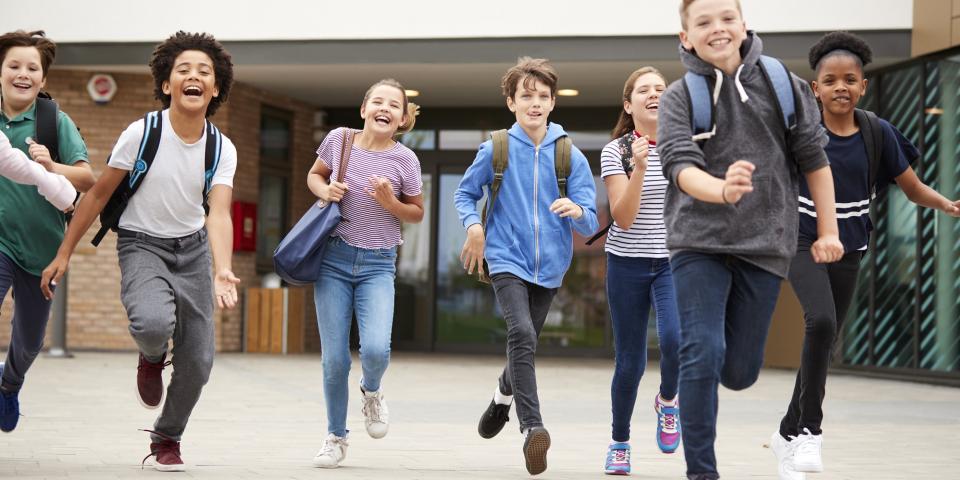 Gruppe von Schülerinnen und Schülern verlässt fröhlich rennend ein Schulgebäude.