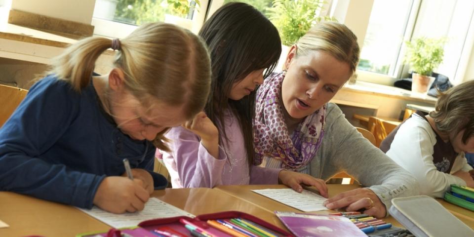 Eine Lehrerin sitzt zwischen Grundschülerinnen und erklärt etwas.