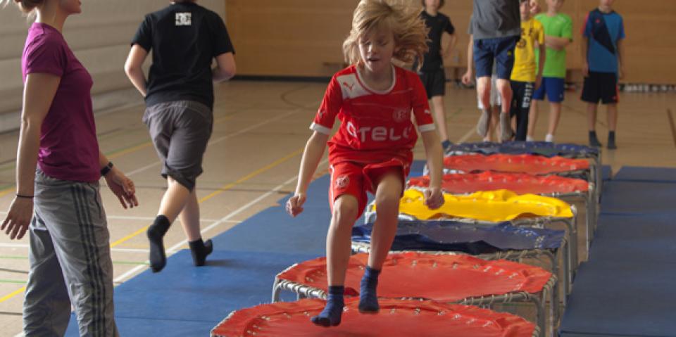 Kinder springen im Sportunterricht auf Minitrampolinen.