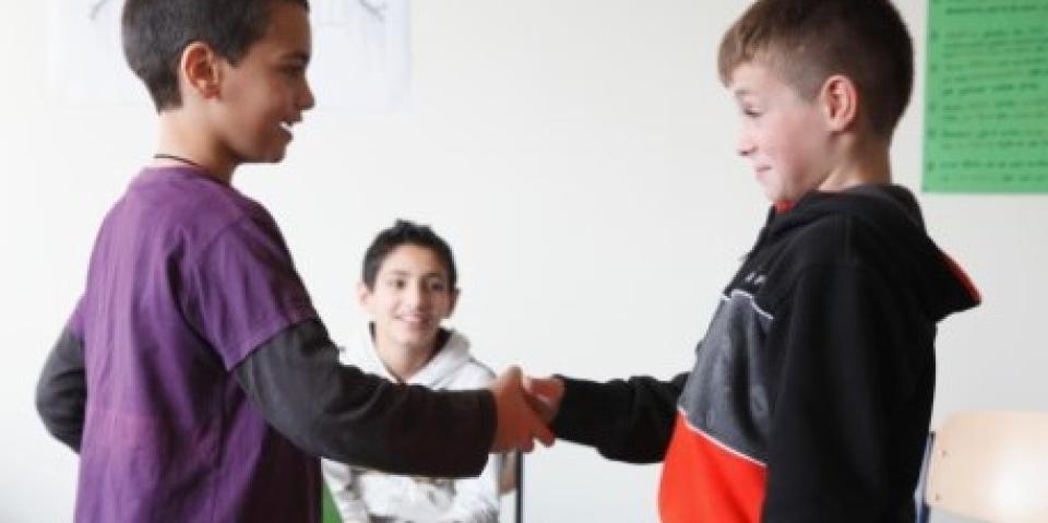 Zwei Jungen schütteln sich die Hände. Ein weiterer schaut zu.