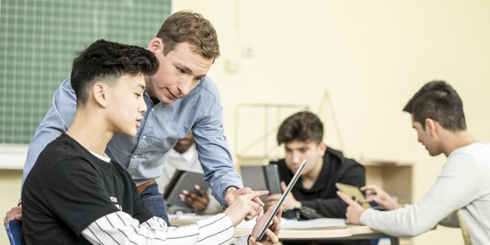 Schüler und Lehrer blicken gemeinsam auf ein Tablet.