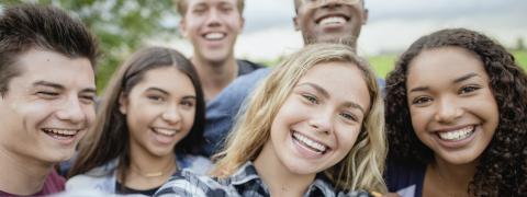 Selfie-Perspektive auf mehrere junge Menschen, die sich lächelnd zum Foto gruppiert hat.