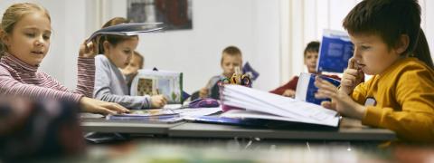 Grundschülerinnen und Grundschüler sitzen während des Unterrichts vor aufgeschlagenen Büchern, lesen und arbeiten.