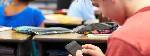 Ein Schüler sitzt im Unterricht und blickt auf das Handy in seiner Hand.