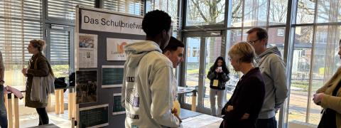 Schulministerin Feller steht mit Schülerinnen und Schülern vor einem Stand der Regionalen Lernstatt NRW über die Schulbriefwahl.