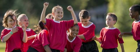 Kinder in Sport-Trikots stehen jubelnd zusammen.
