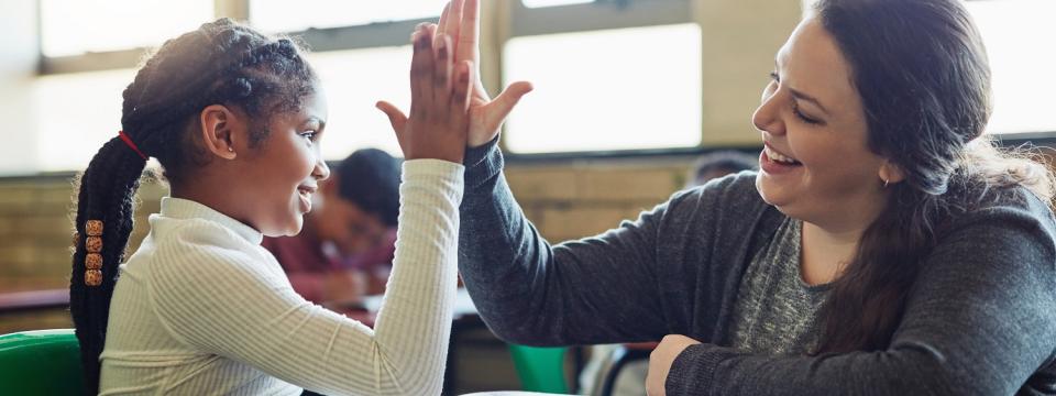 Schülerin und Lehrerin berühren ihre Hände in einer "High Five"-Geste. Beide lächeln dabei.
