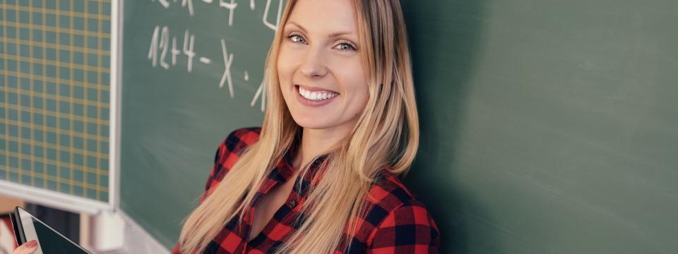 Eine Lehrerin steht mit dem Rücken zur Tafel, in ihren Händen hält sie einen Tablet-Computer.